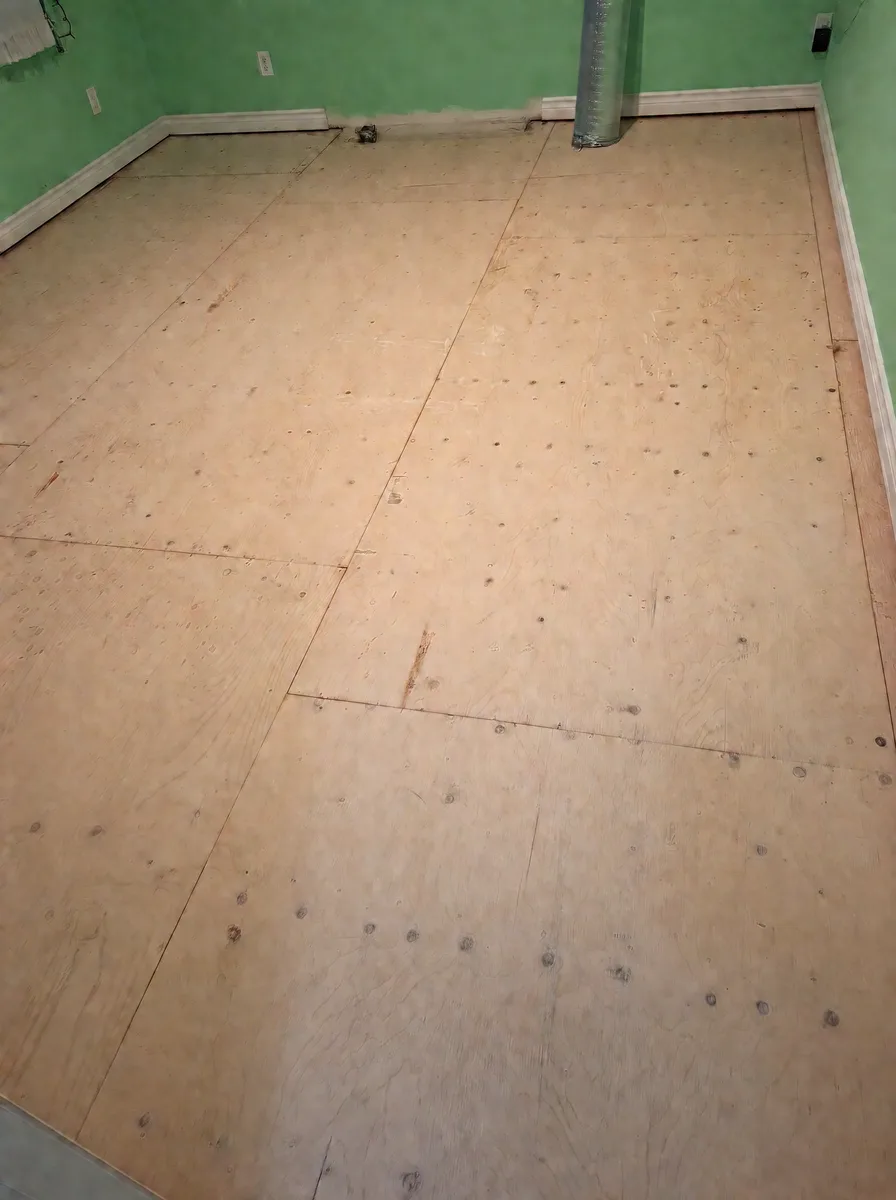 Bedroom with mint-green walls stripped to the plywood subfloor before new flooring