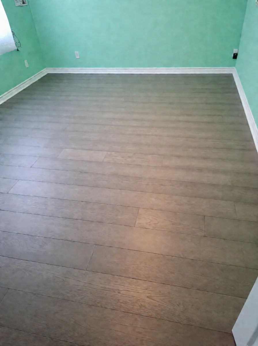 Mint-green bedroom finished with grey-brown wide-plank oak flooring and white baseboard