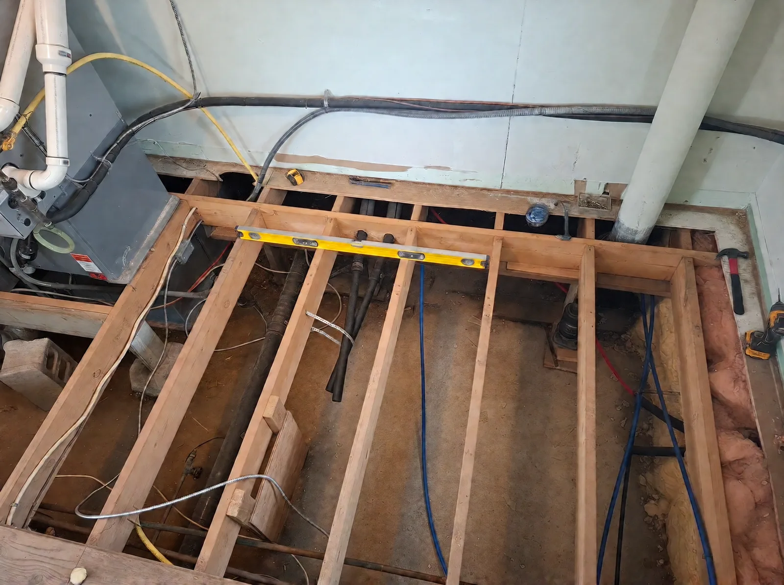 New floor joists framed with PEX water lines and a level across the laundry-room floor