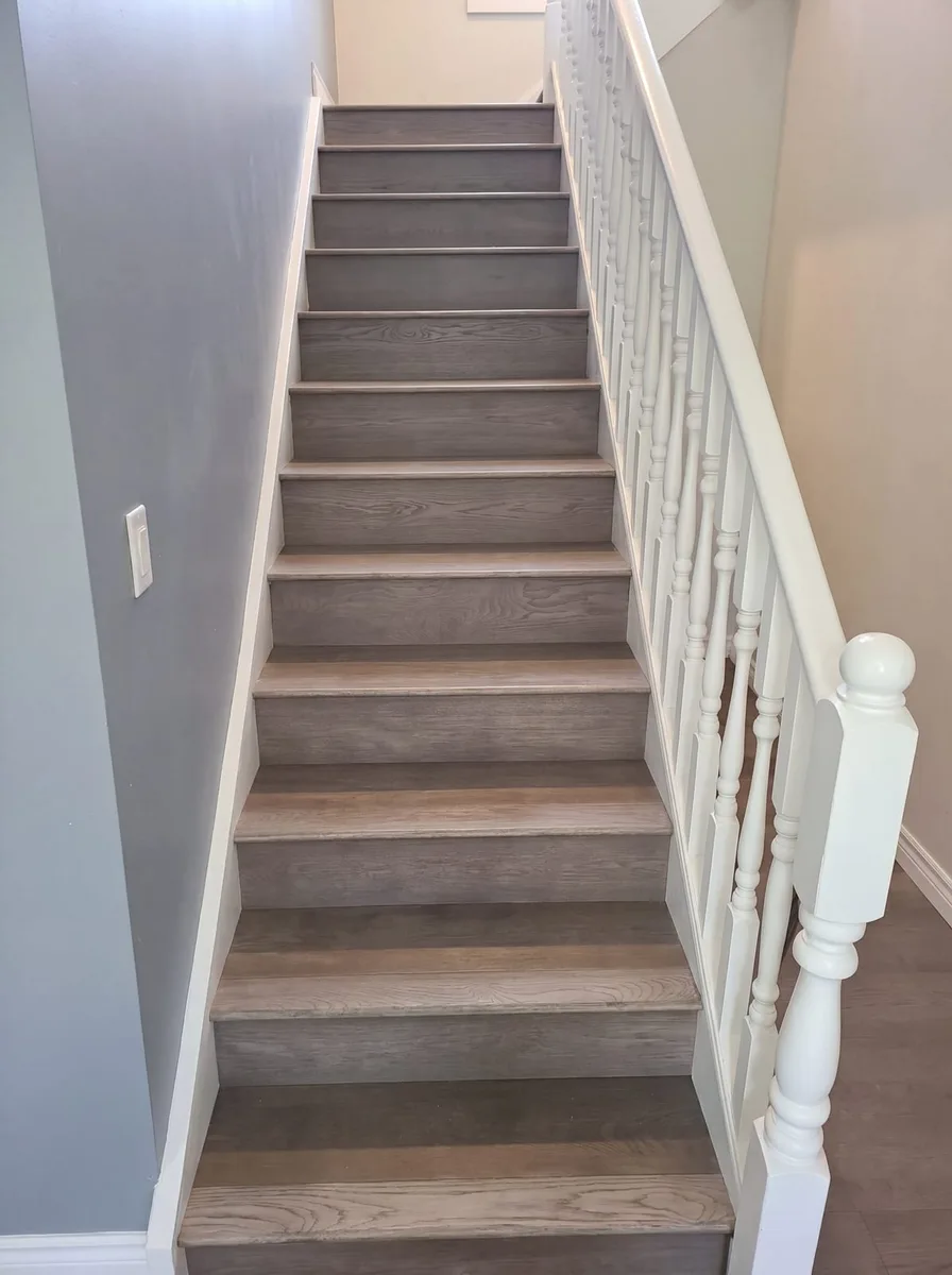 Staircase with new grey-brown oak treads beside a white spindle railing