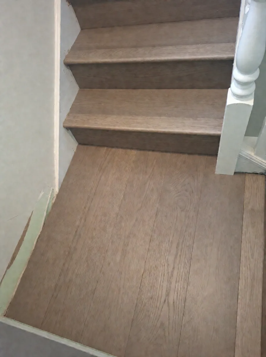Close-up of new oak stair treads meeting the oak-floored landing beside a white newel post