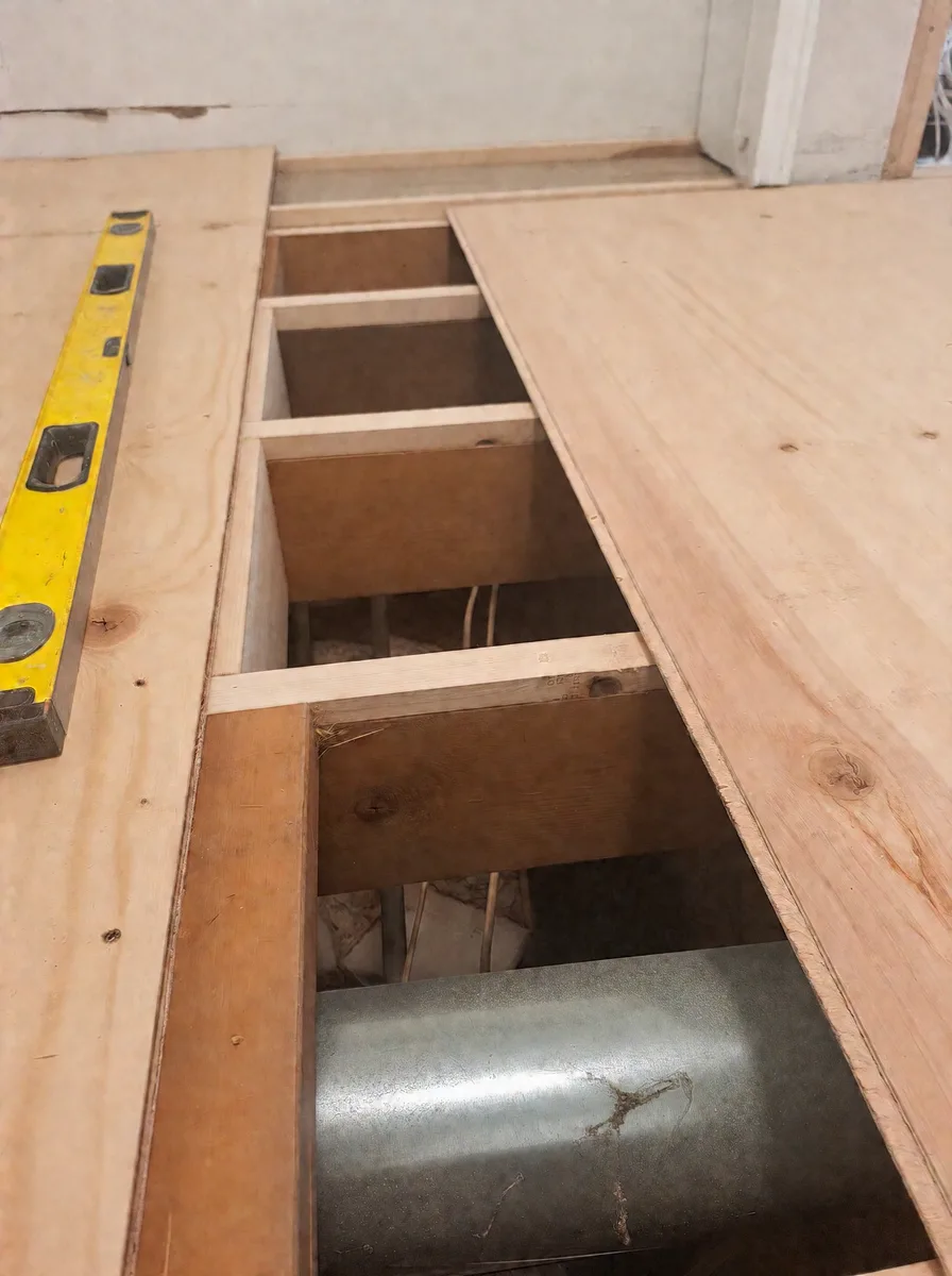 Bedroom floor opened to the joists with the heating duct exposed beside new plywood