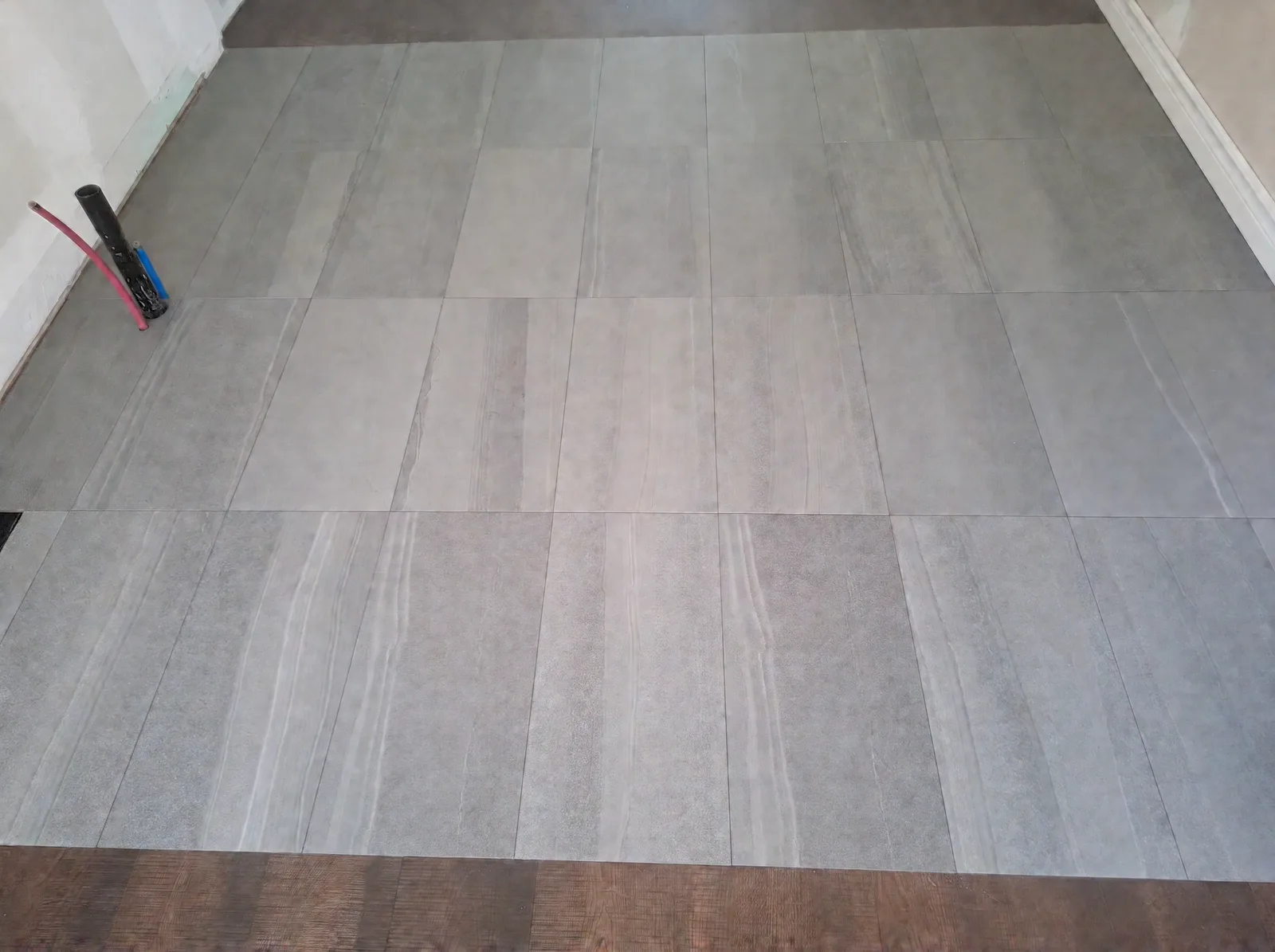 Large-format grey stone-look tile meeting dark brown plank flooring