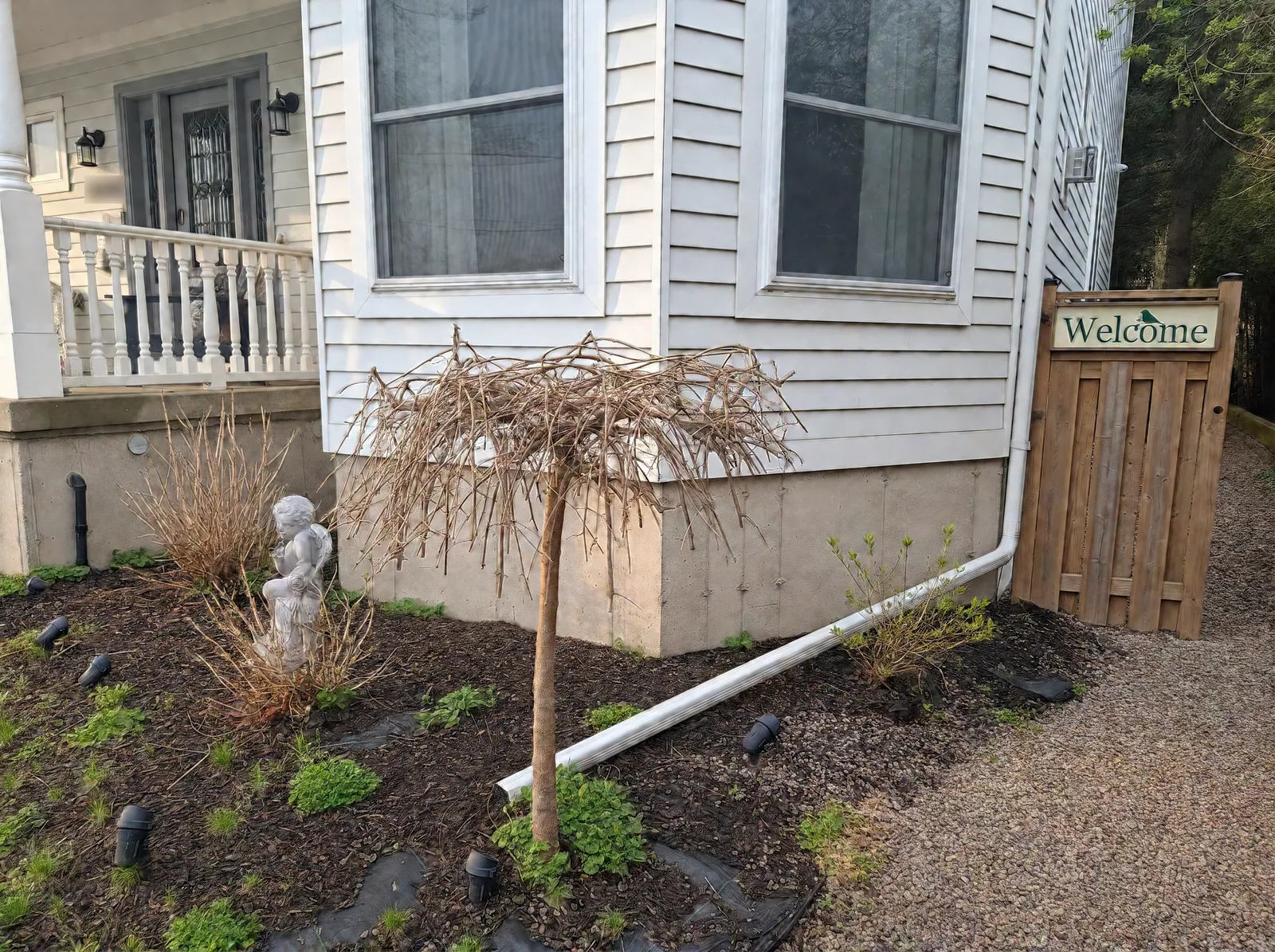 Bare light-grey concrete foundation at the front corner of the house before parging, beside a wooden Welcome gate