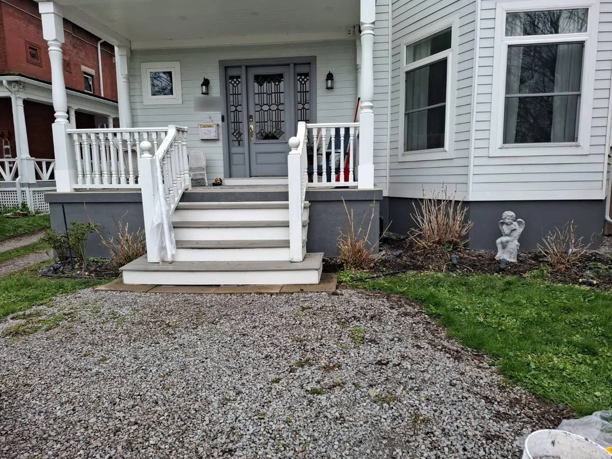 Front porch with white turned-baluster railings, grey composite steps and a charcoal parged foundation skirt