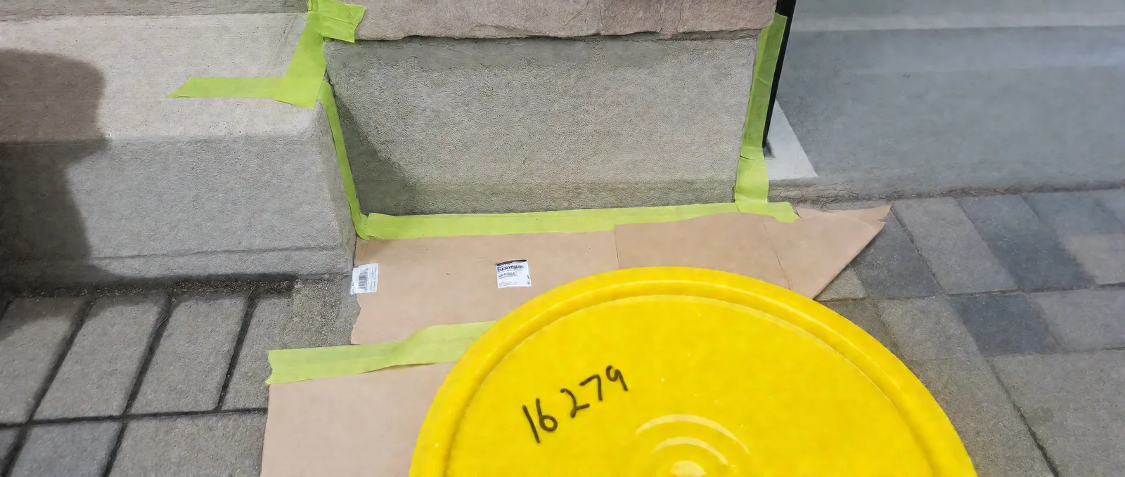 Concrete foundation beside an entry step outlined with green masking tape, with paper covering the pavers during parging preparation