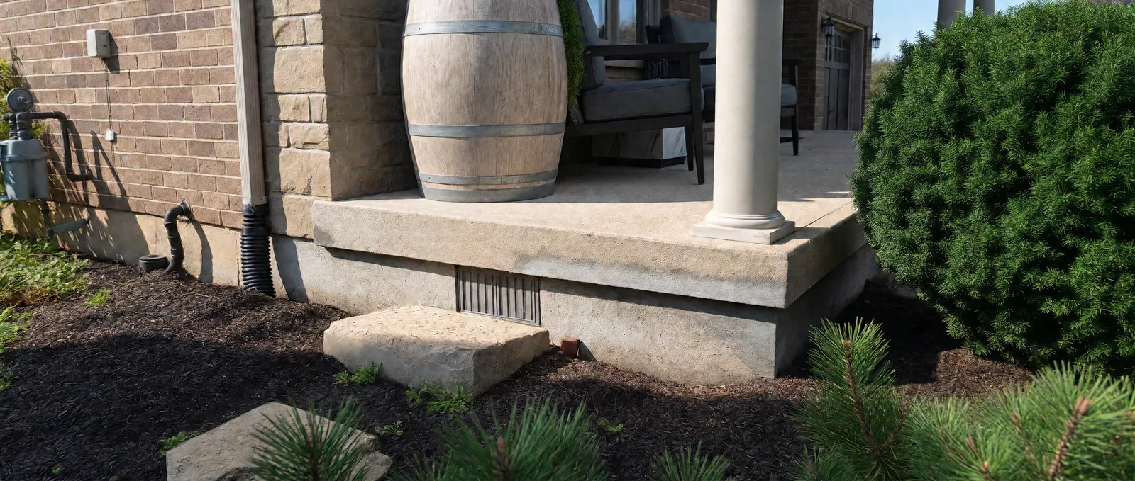 Parge finish beneath a concrete porch slab, around a rectangular foundation vent and beside a landscaped garden bed