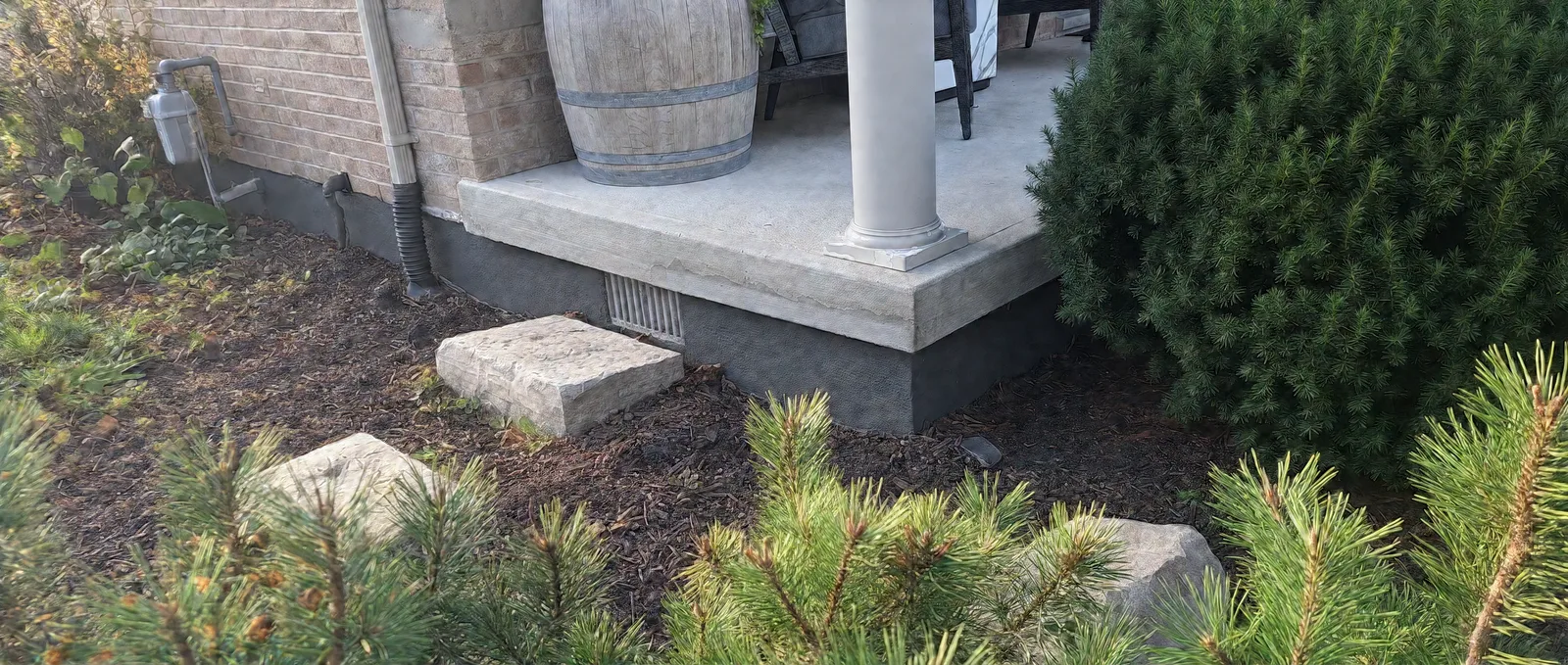 Charcoal parge finish wrapping the corner of a porch foundation beneath a white column, with a vent and garden stones alongside